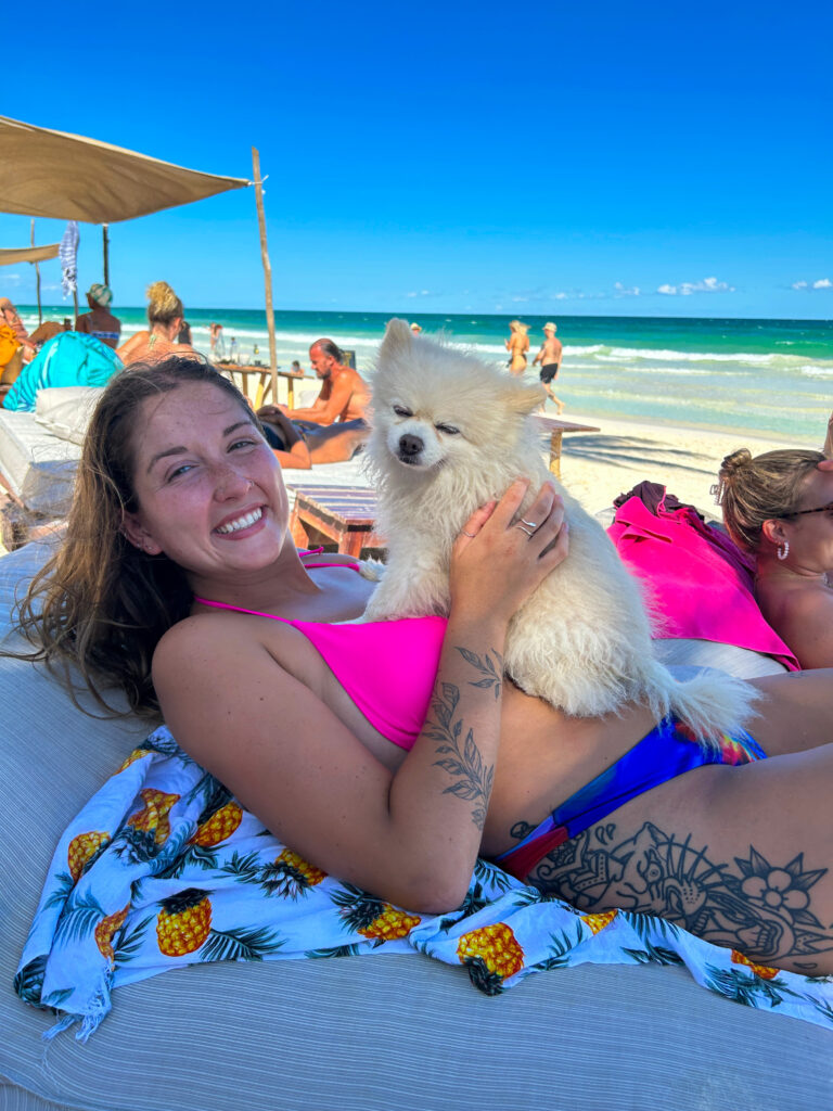 Aly holding a white fluffy dog on the beach